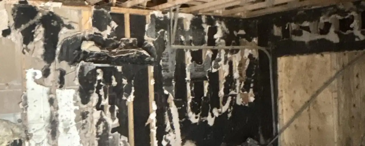 A burned-out room with charred wall studs and the roof trusses exposed after a house fire