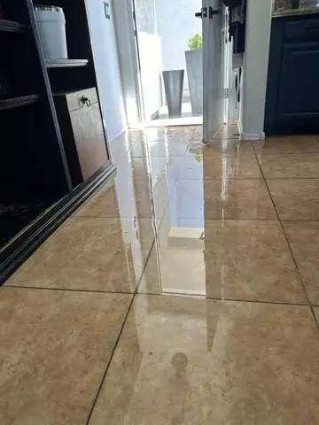 Standing water spread across a tile floor inside a home after a water leak