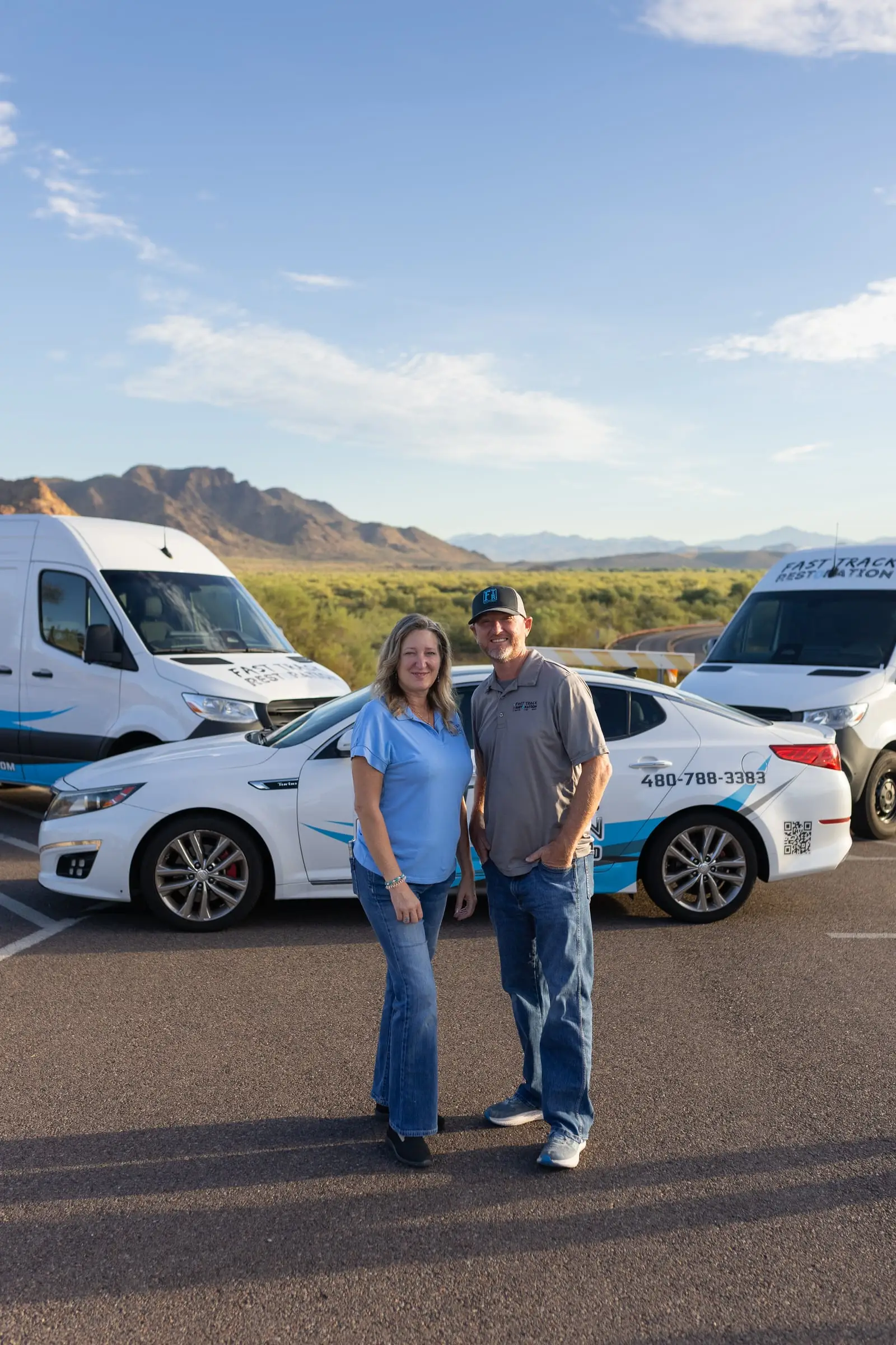 Fast Track Restoration co-founders Becci Stoflet and Brian Bradford standing in front of the company car and vans