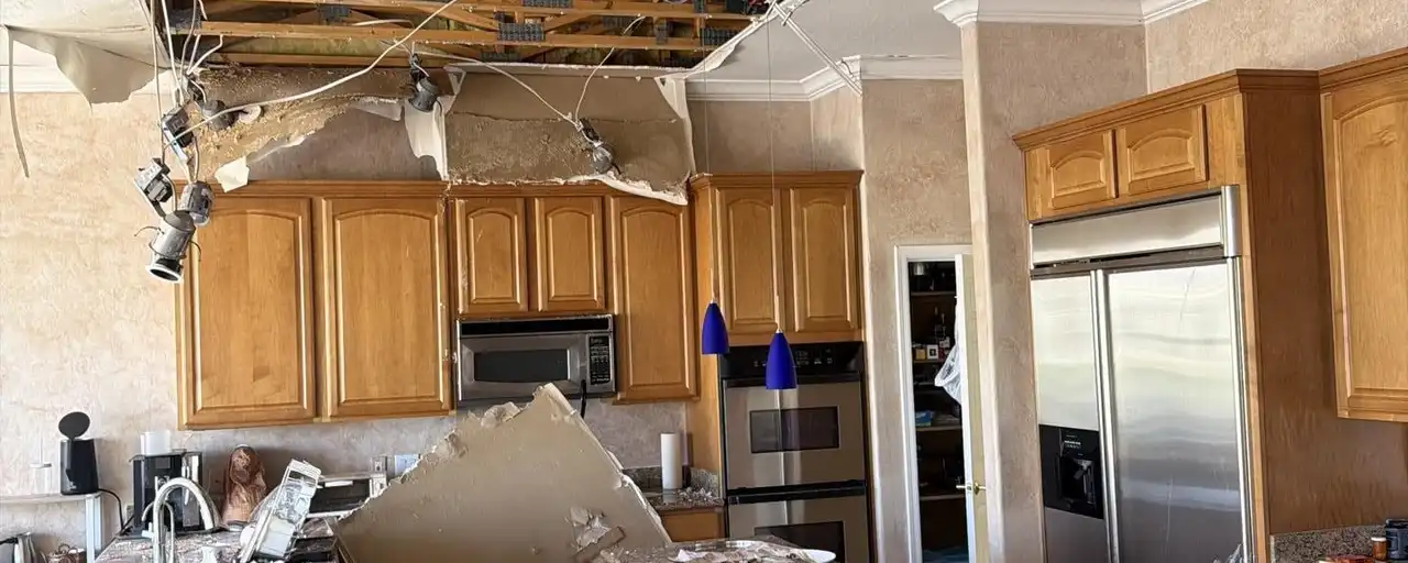 A kitchen ceiling collapsed onto the counters and floor, with the insulation down and the roof framing exposed